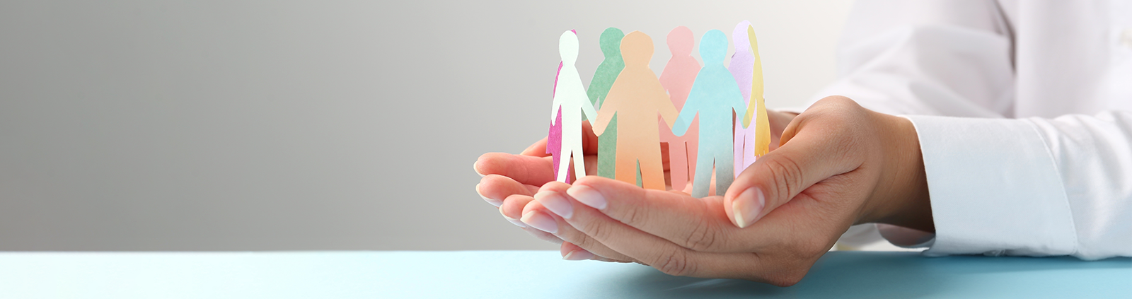 Hands holding group of coloured paper cutouts of people