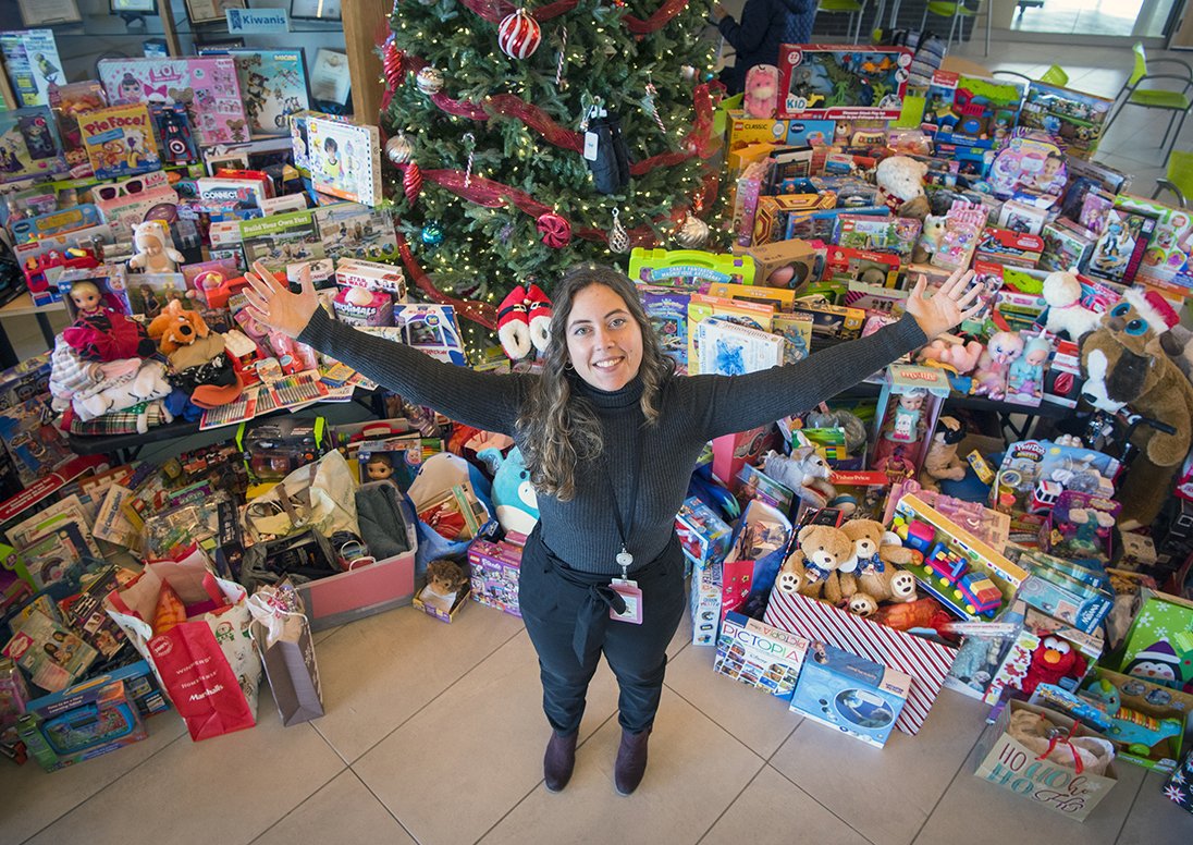 City employee holds out arms in front of gifts donated as part of the Tree of Giving campaign