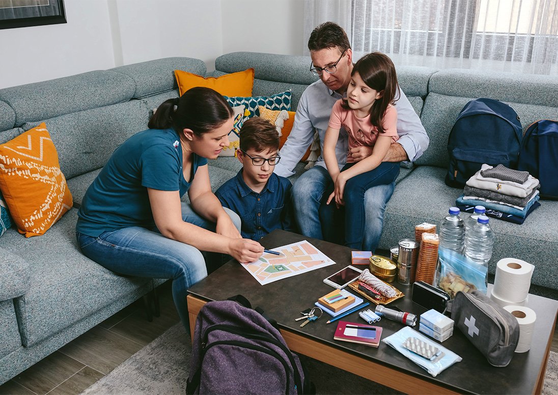 A family goes through their emergency kit checklist with emergency supplies on their coffee table.