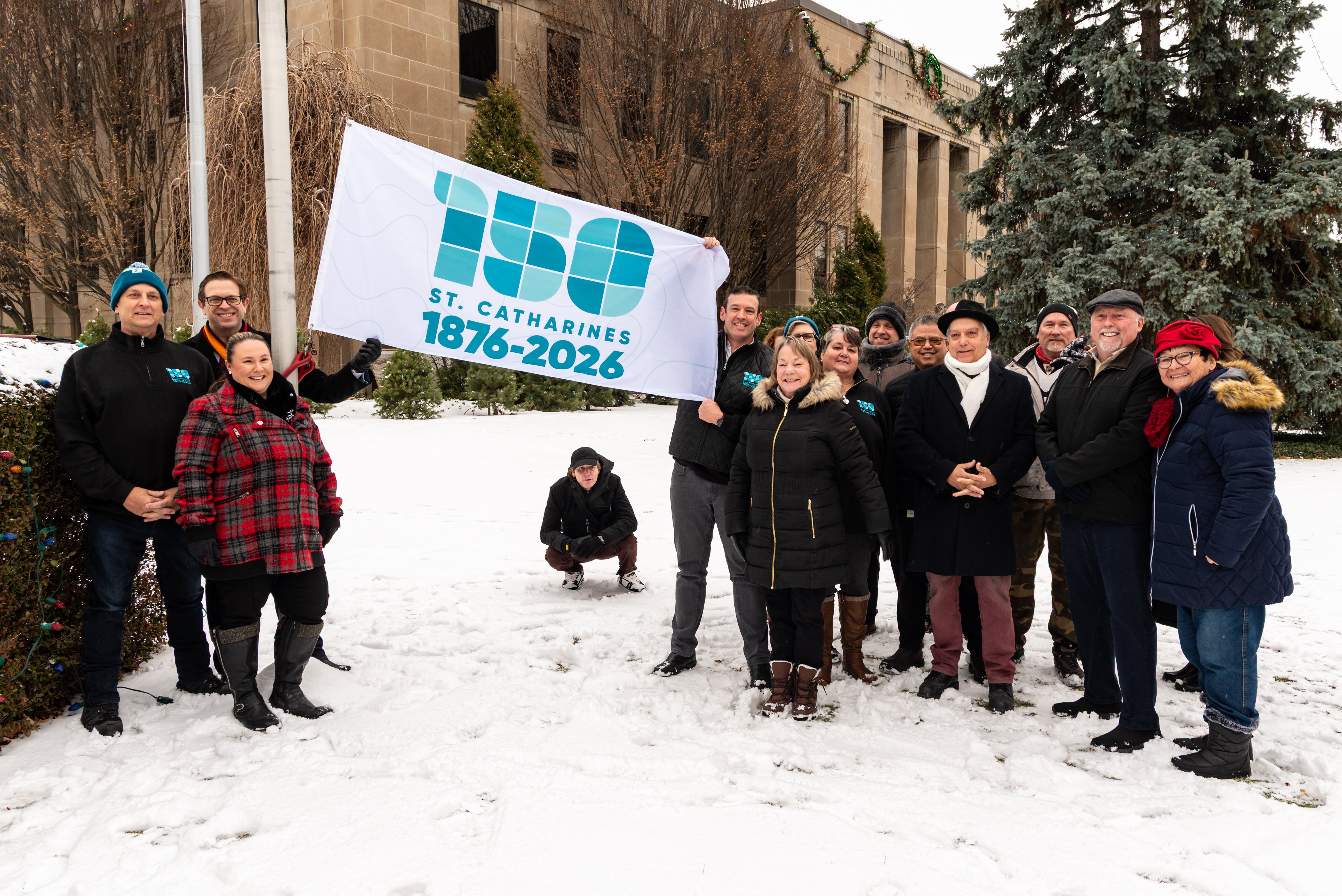 A group of people gather and pose with a flag bearing the number 150 to mark St. Catharines' 150th anniversary as a City.