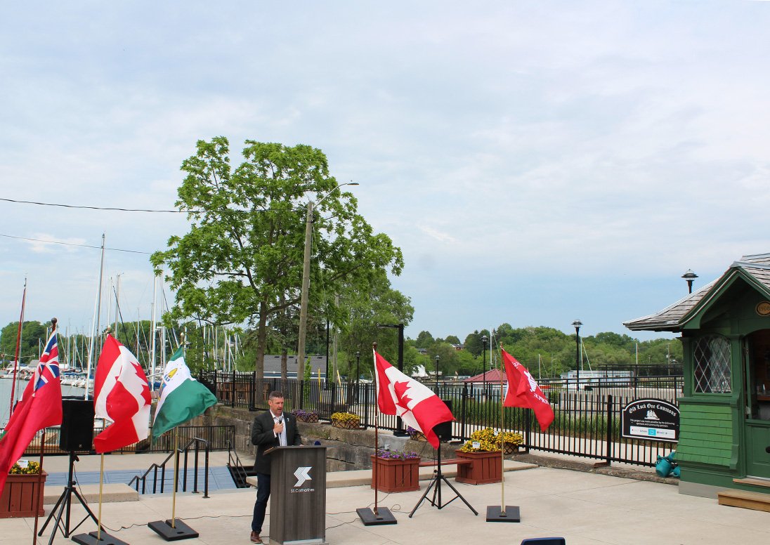 An overview photo of the Old Lock One Commons area with the Mayor speaking during the naming ribbon cutting and official sign unveiling An overview photo of the Old Lock One Commons area with the Mayor speaking during the naming ribbon cutting and official sign unveiling