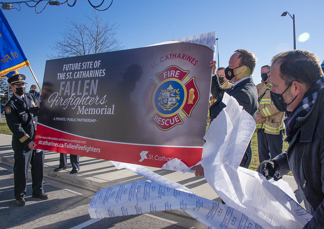 Two firefighters holding a sign announcing the memorial location as it is revealed