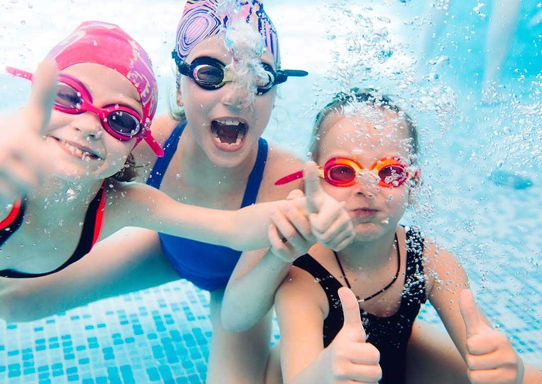 Three little girls giving thumbs up while swimming under water.