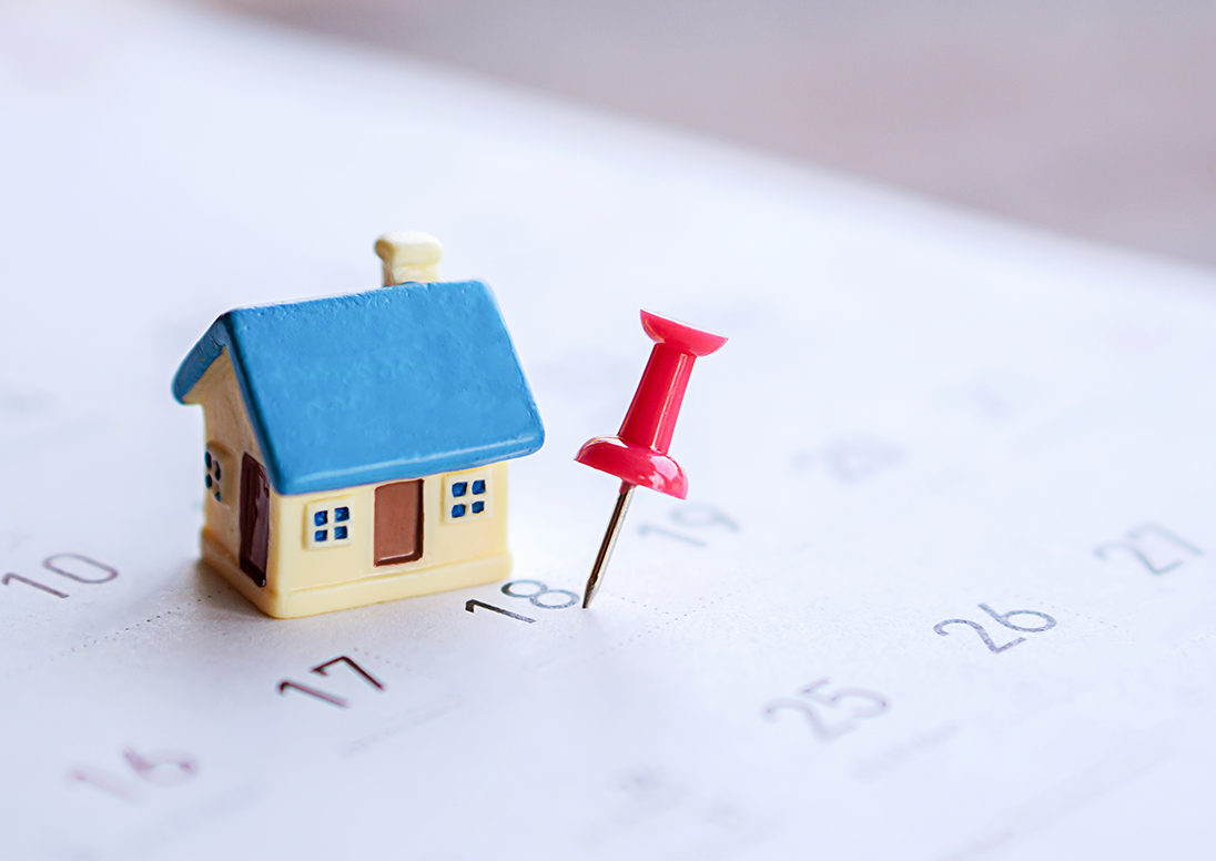 A small toy house sitting on a calendar with a red pin