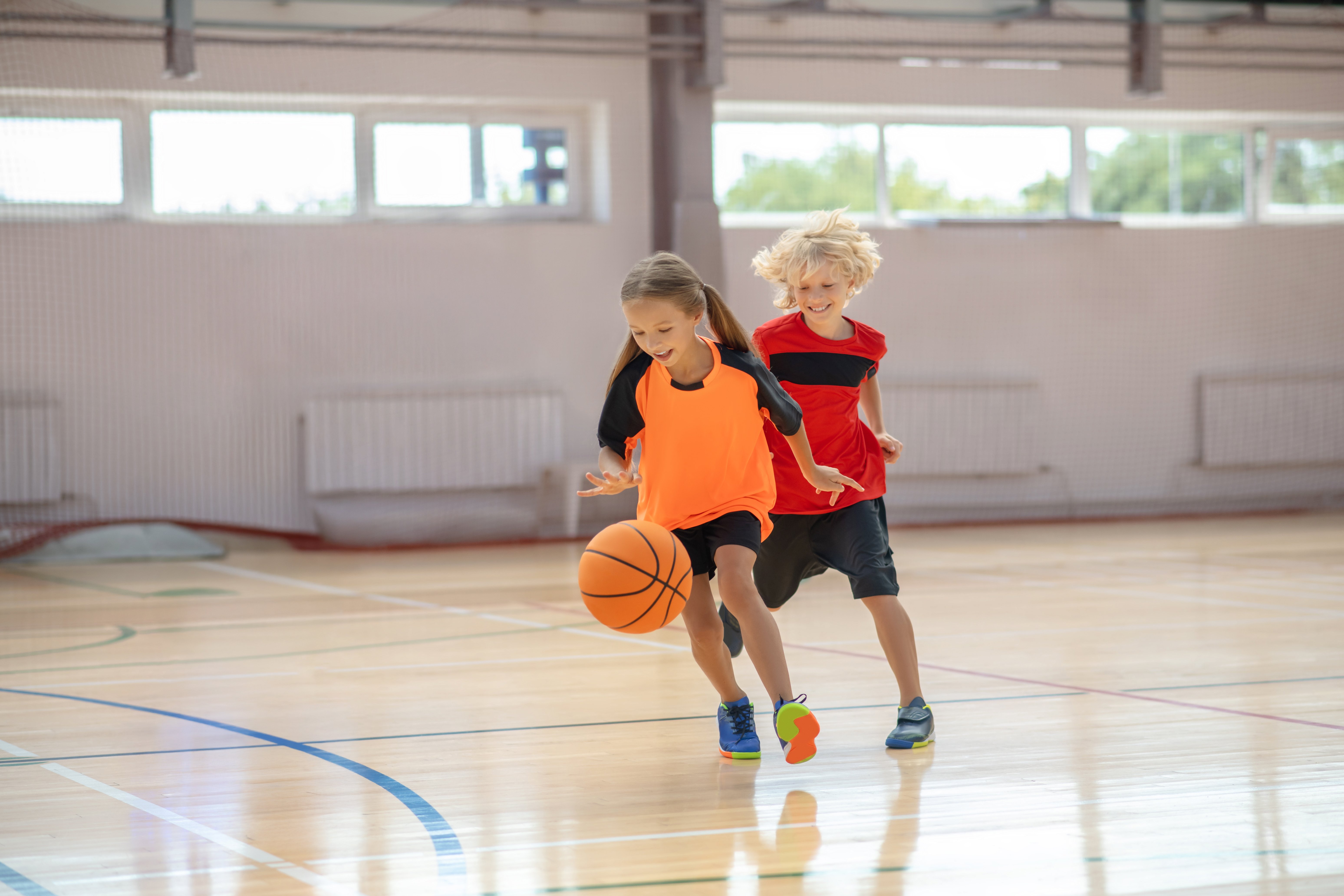 Two kids playing basketball in a gymnasium.