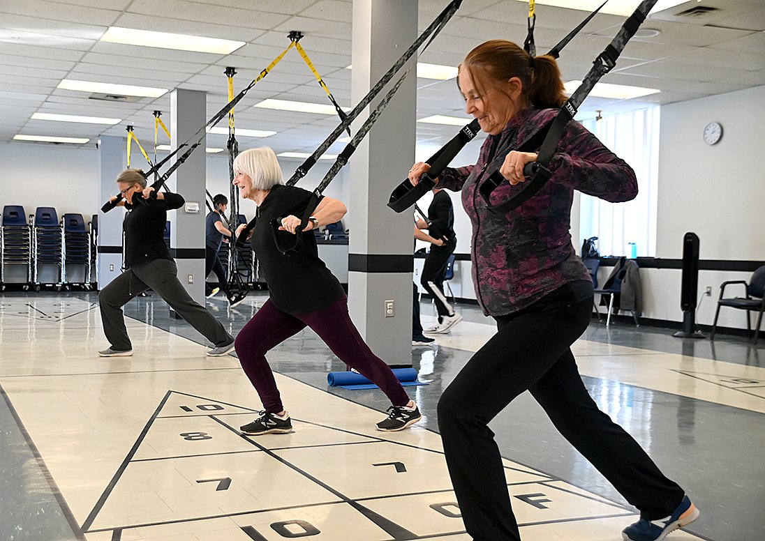 Participants pull down on resistance bands during a TRX class in a gymnasium.