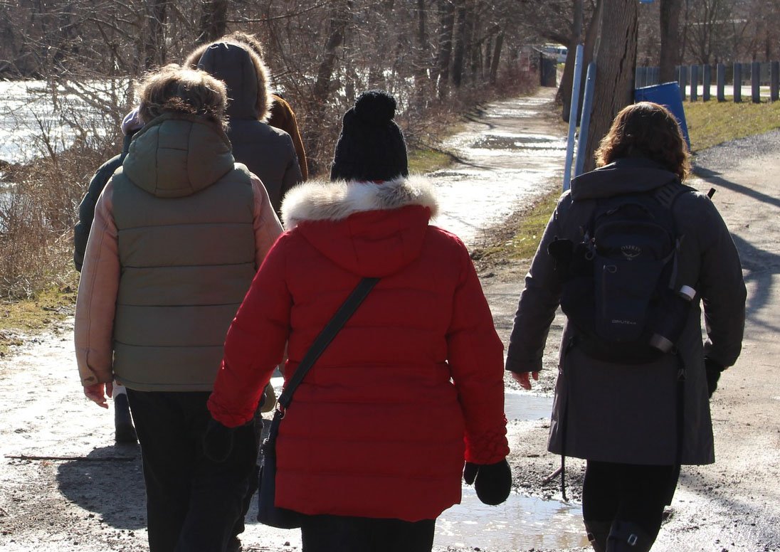 People walk outdoors along a river during a St. Catharines Museum and Canal Centre's staff-guided community walk.