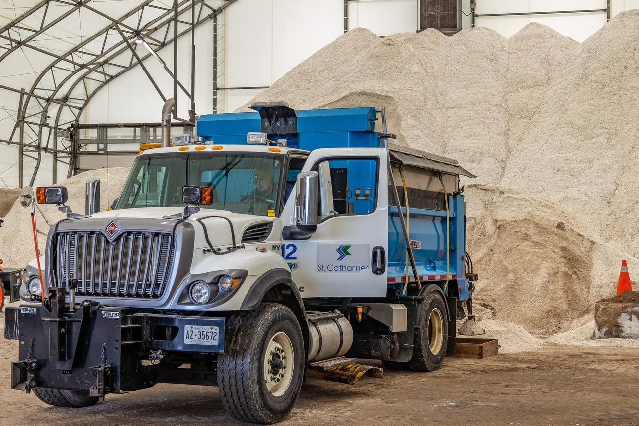A large plow truck sits in front of a large pile of road salt.
