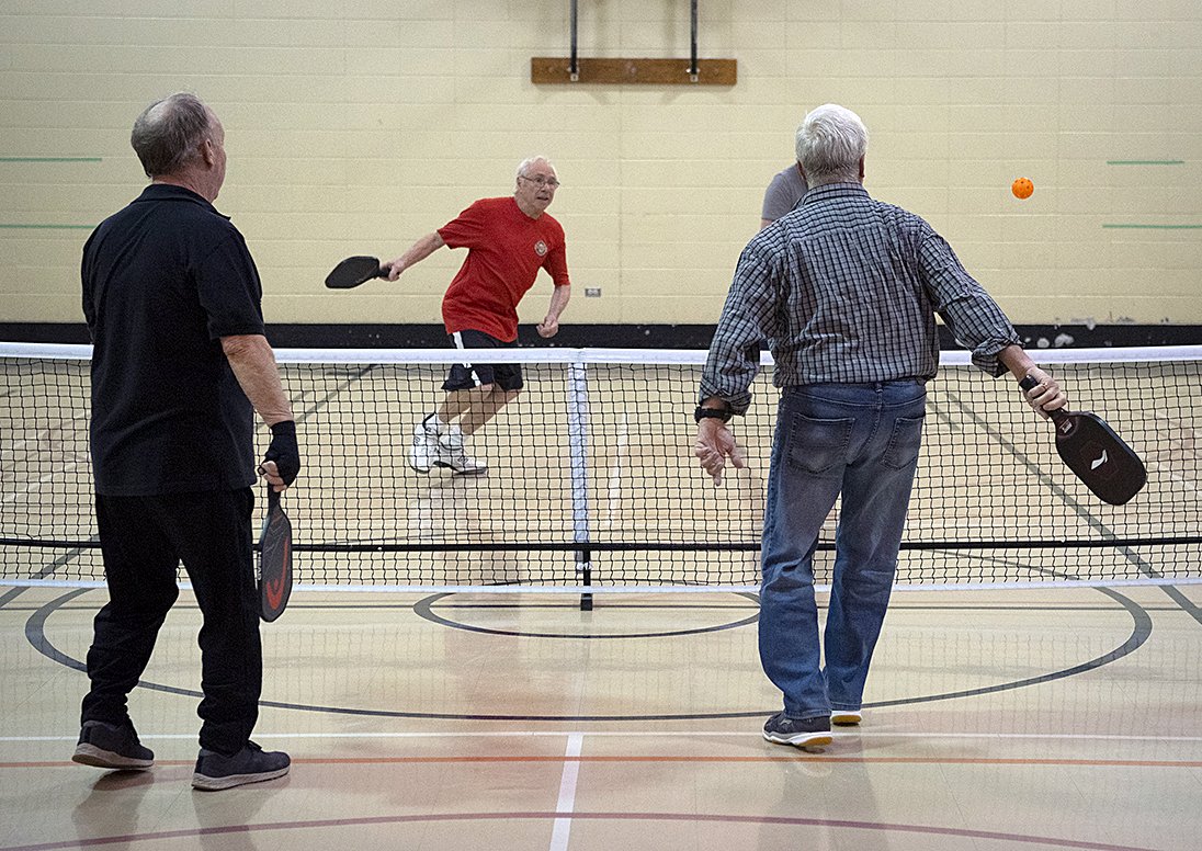 Three men playing pickleball in a gymnasium