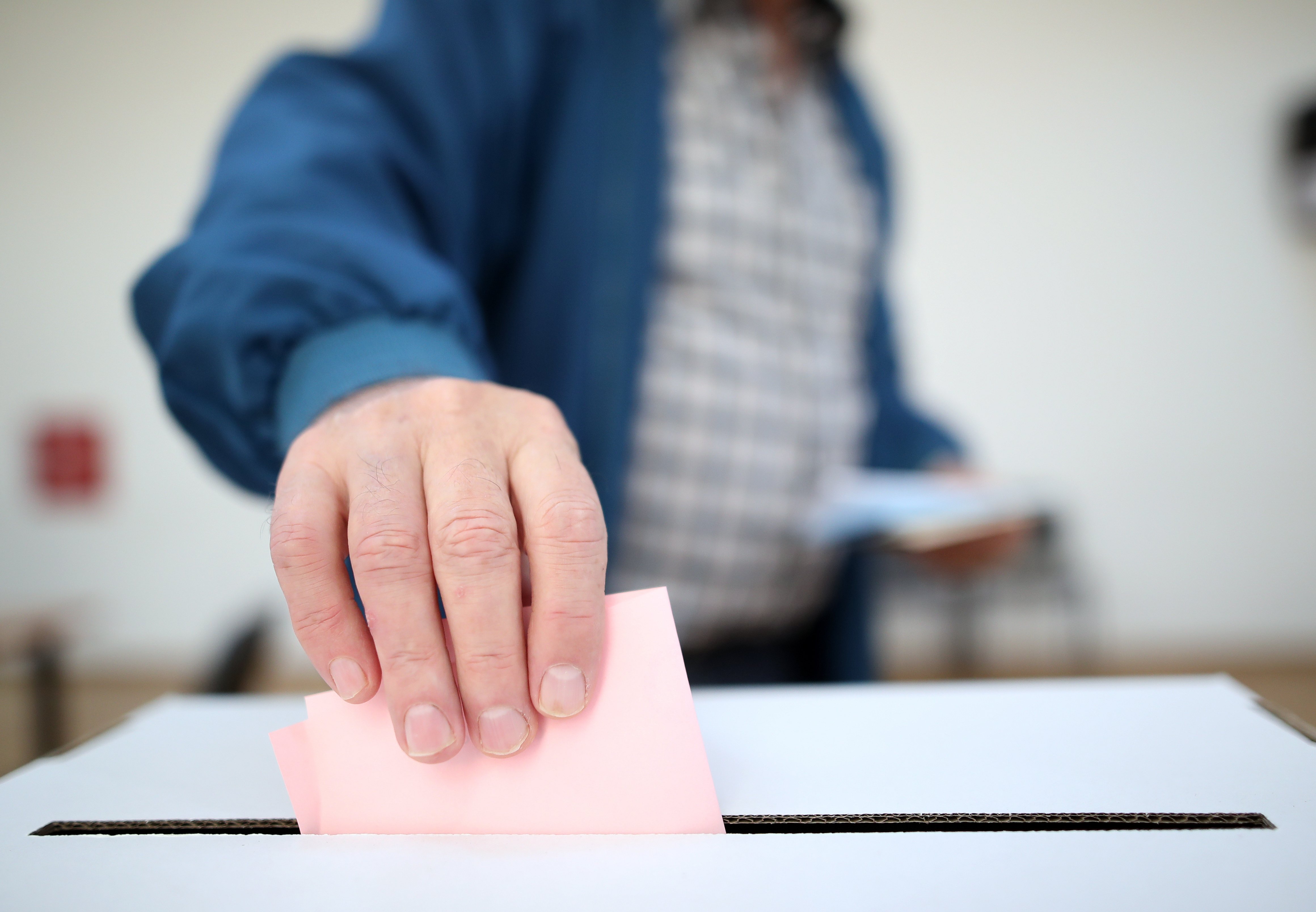 A hand places a ballot in a box