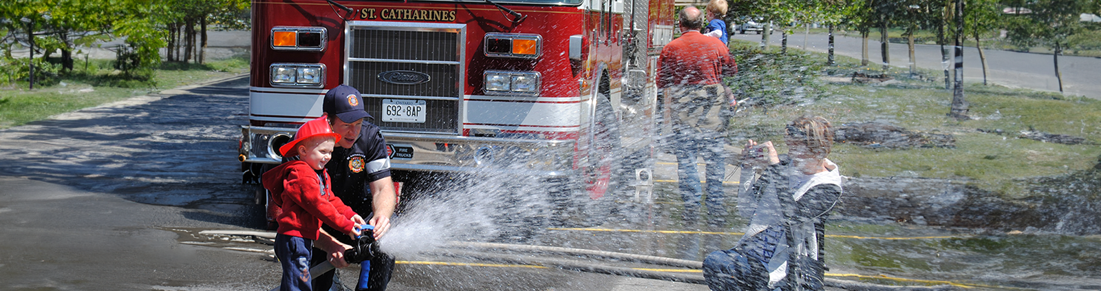 A St. Catharines Firefighter spraying a hose with a child 