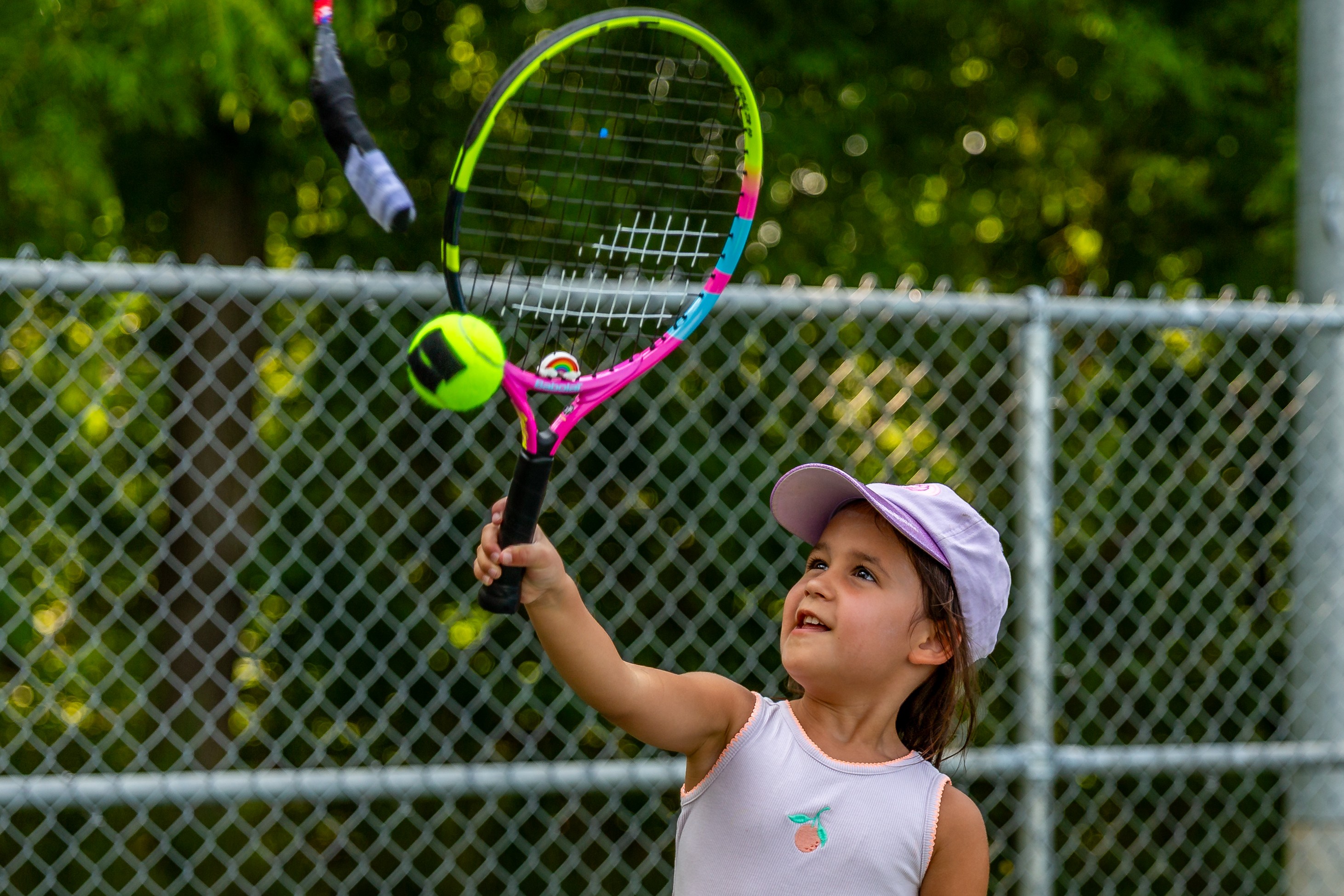 Little girl looking up hits a tennis ball with her colourful tennis racket.